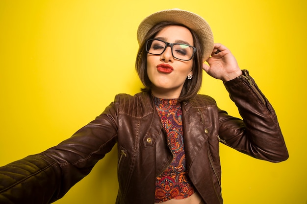 Retrato de una hermosa mujer sonriente exitosa haciendo selfie en una pared amarilla