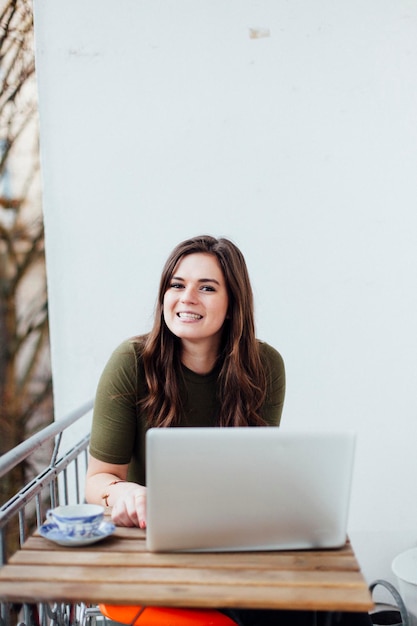 Retrato de una hermosa mujer sonriente sentada junto a una computadora portátil en el balcón