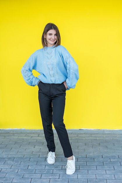 Retrato de hermosa mujer sonriente en suéter azul sobre pared amarilla