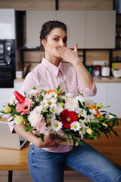 Retrato hermosa mujer sosteniendo una composición de flores posando en la cocina blanca en casa Floristería presentando una canasta con flores de colores