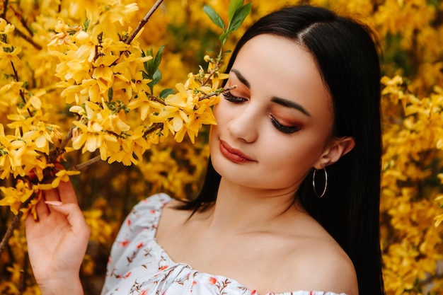 Retrato de hermosa mujer tierna vestida con un vestido florido rosa posando cerca del árbol de forsythia amarilla