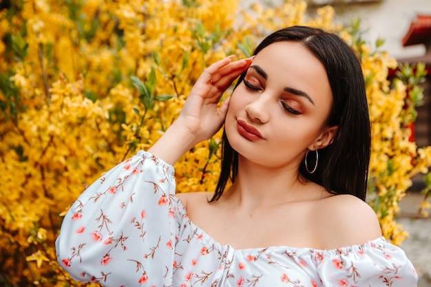 Retrato de hermosa mujer tierna vestida con un vestido florido rosa posando cerca del árbol de forsythia amarilla