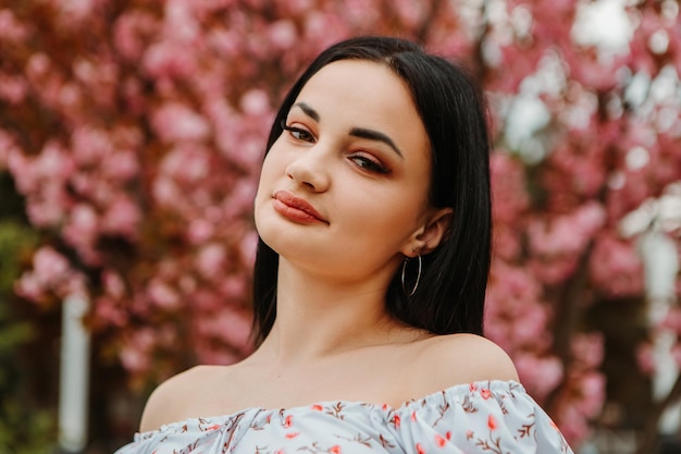 Retrato de una hermosa mujer tierna vestida con un vestido florido rosa posando cerca de las flores de cerezo de sakura