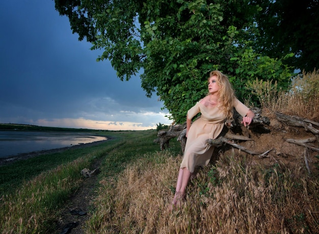 Retrato de una hermosa mujer triste en la orilla del río al atardecer