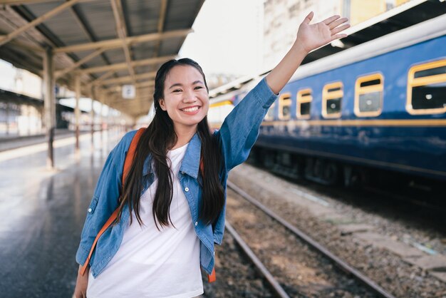 Retrato hermosa mujer viajero turista mano ola paquete de bolsa en la estación de tren