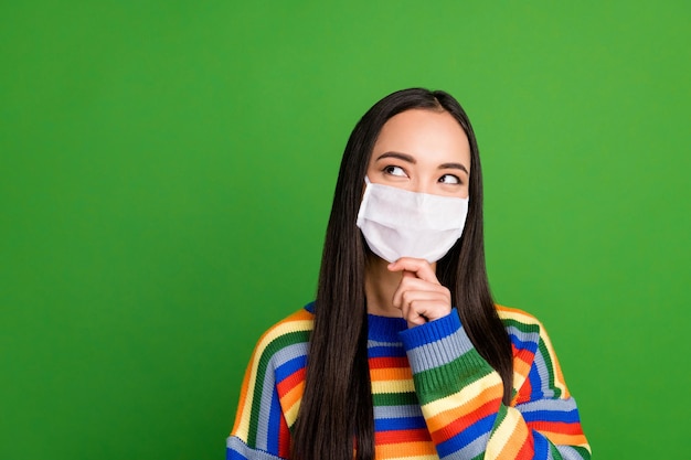 Retrato de hermosa niña alegre pensativa desgaste jersey de rayas máscara médica aislada sobre fondo de color verde