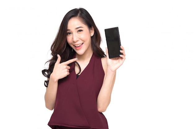 Retrato de una hermosa niña alegre con vestido rojo y mostrando o presentando la aplicación de teléfono móvil y señalando con el dedo al teléfono inteligente en la mano