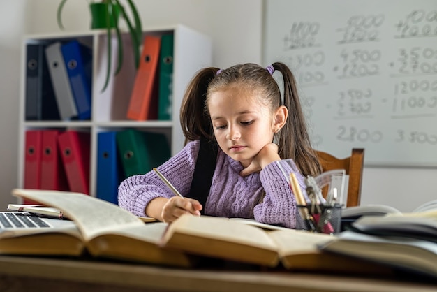 Retrato de una hermosa niña en el aula en un escritorio con libros y útiles escolares