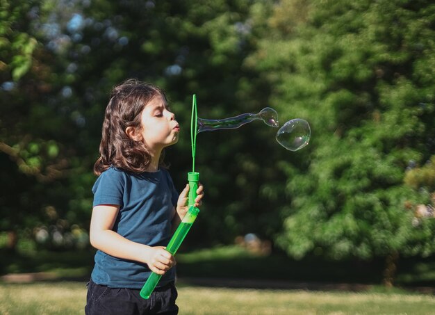 Retrato de una hermosa niña caucásica sopla pompas de jabón de pie en el parque