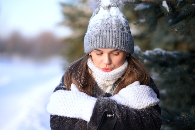 Retrato de una hermosa niña congelada, una joven congelada parada en la nieve en un día frío de nieve en invierno en un parque o bosque con ropa abrigada, sombrero, bufanda y guantes, sufriendo, temblando debido a la baja temperatura