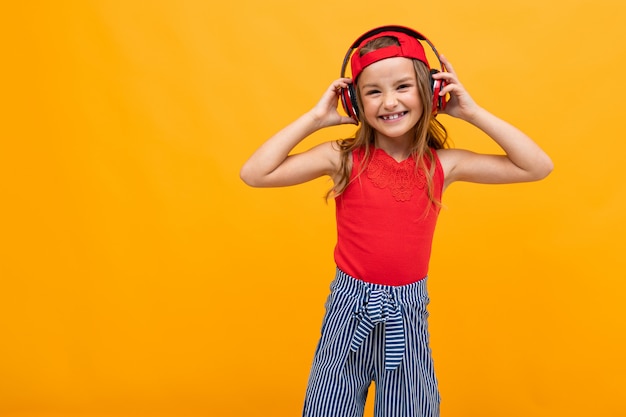 Retrato de una hermosa niña encantadora en un look casual con auriculares rojos sale a la música en una naranja con espacio de copia