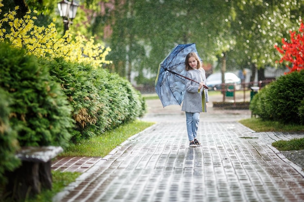 Retrato de una hermosa niña con estilo con un paraguas bajo la lluvia en el parque de la ciudad