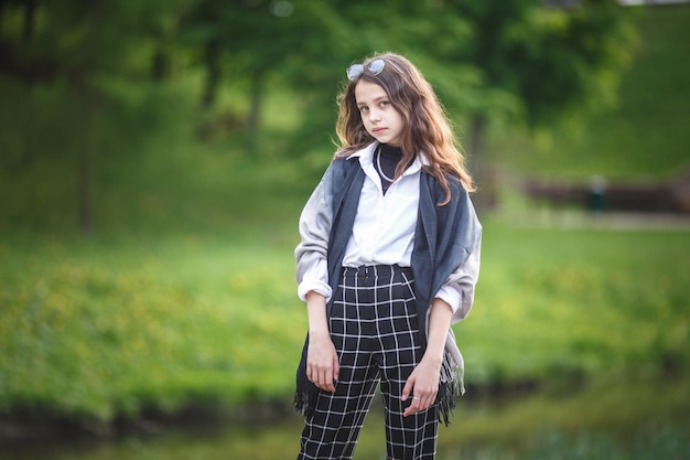 Retrato de una hermosa niña con estilo en el parque de la ciudad en el fondo del bosque verde