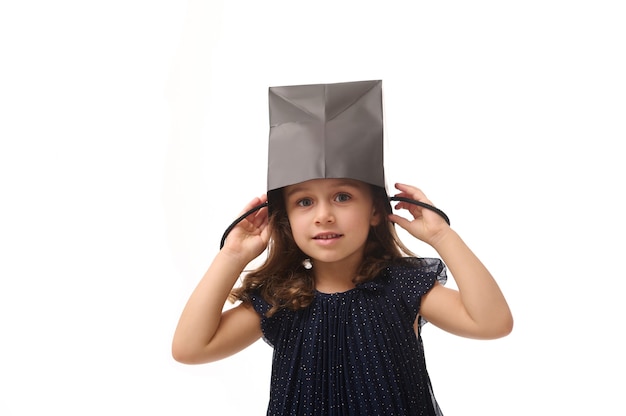 Retrato de hermosa niña europea caucásica divirtiéndose, poniendo un paquete de compras negro en la cabeza, mirando a cámara, aislado sobre fondo rosa con espacio de copia, concepto de Viernes Negro