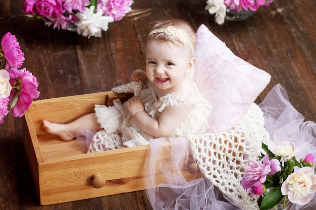 Retrato de una hermosa niña con flores rosas. Dulce niña sonriente sentada en una caja de madera en el suelo