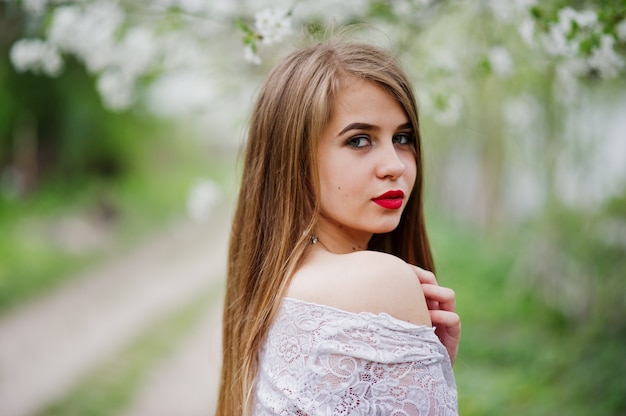 Retrato de hermosa niña con labios rojos en el jardín de flores de primavera, use vestido rojo y blusa blanca