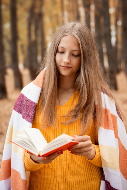 Retrato de una hermosa niña leyendo un libro mientras pasea por un colorido parque de otoño