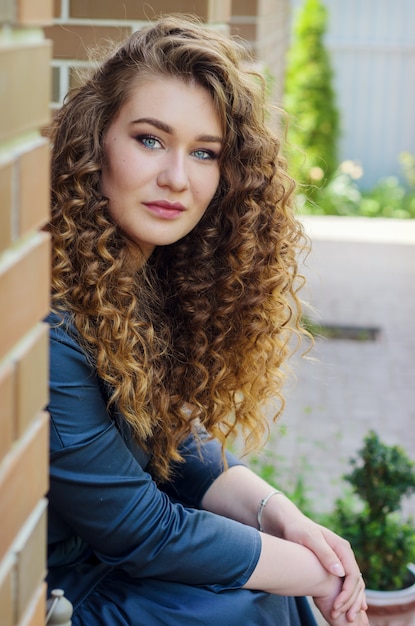 Retrato de una hermosa niña linda con el pelo rizado elegante contra una pared de ladrillos de una casa de campo.