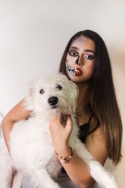 Foto retrato de una hermosa niña en maquillaje de halloween con su perro sobre fondo blanco.