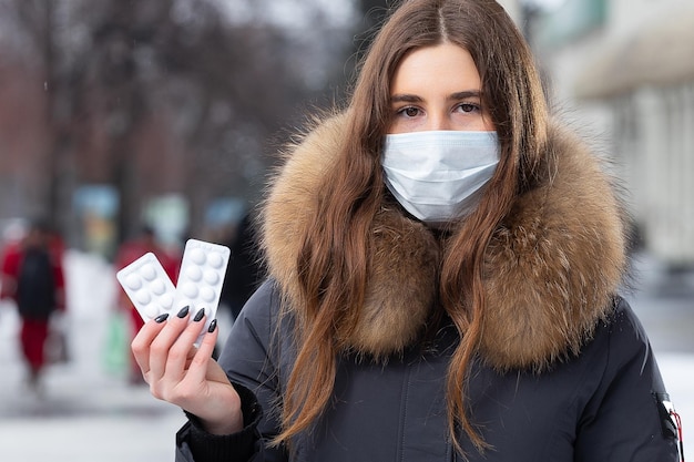 Retrato de una hermosa niña con una máscara de protección médica sosteniendo pastillas blancas en sus manos para los resfriados y la gripe Retrato de una mujer en la calle de invierno bajo la nieve