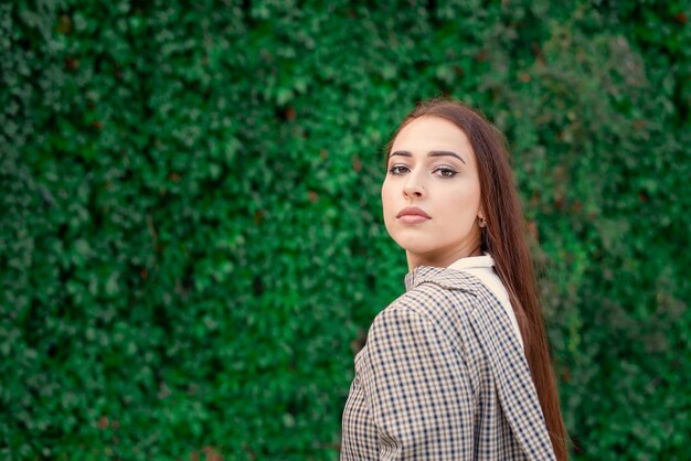 Retrato de una hermosa niña del Medio Oriente en el contexto de una pared de plantas verdes.