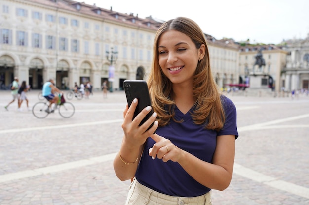 Retrato de una hermosa niña moderna sonriente con un teléfono móvil en la plaza de la ciudad vieja