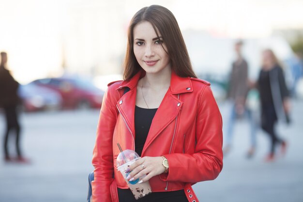 Retrato de hermosa niña morena caminando por la calle. Mantener bebida para llevar en una mano