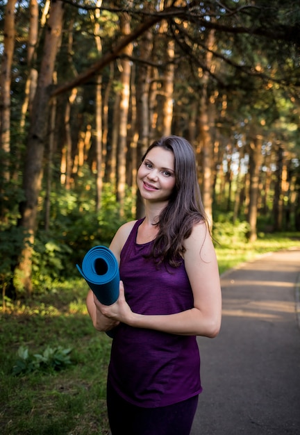 Retrato de una hermosa niña morena con una estera de yoga en el camino en el parque