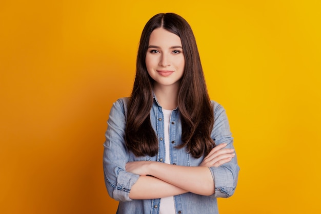 Retrato de hermosa niña morena con las manos cruzadas aisladas sobre fondo amarillo