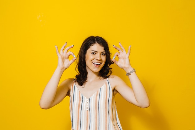 Retrato de una hermosa niña morena sonriendo y mostrando gestos sobre fondo amarillo