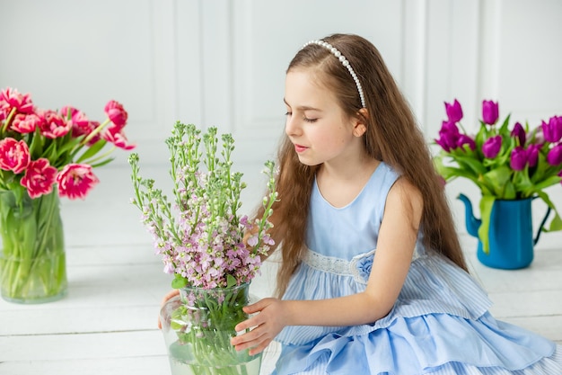 Retrato de una hermosa niña de ojos azules, una niña pequeña con un ramo de tulipanes en una habitación luminosa