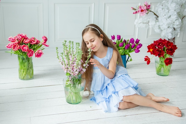 Retrato de una hermosa niña de ojos azules, una niña pequeña con un ramo de tulipanes en una habitación luminosa