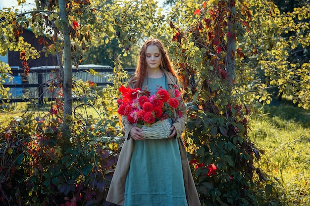 Foto retrato de una hermosa niña pelirroja con flores rojas en un parque de otoño