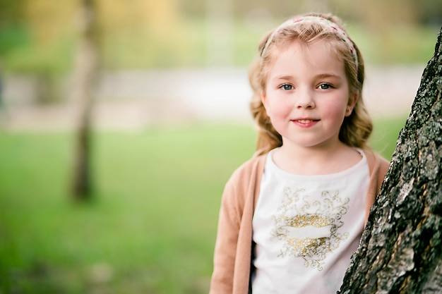 Retrato de hermosa niña de pie cerca de un árbol