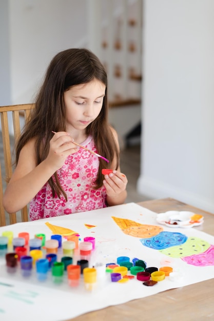 Retrato de una hermosa niña pintando con gouache totalmente concentrada en el proceso creativo Involucrarse plenamente en el proceso de dibujo Gran cantidad de acuarelas y gouache colocados sobre la mesa