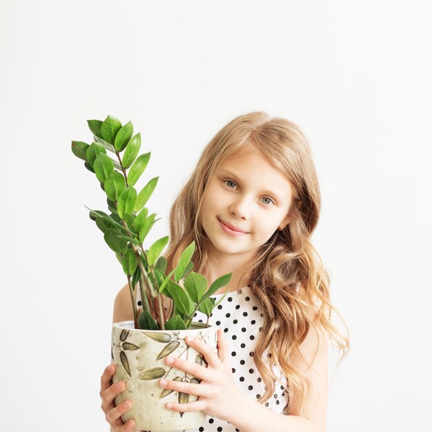 Foto retrato de una hermosa niña con planta de interior verde sobre un fondo blanco.