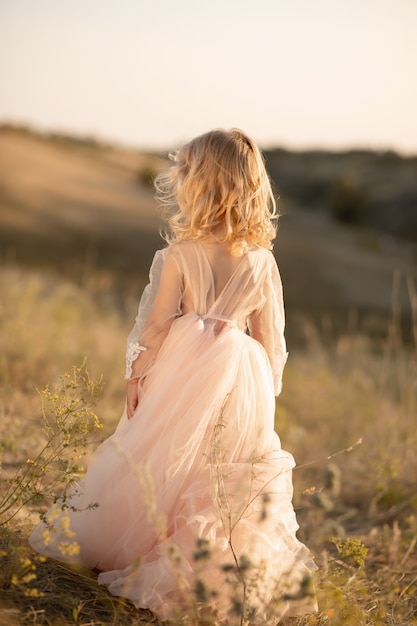 Retrato de una hermosa niña princesa en un vestido rosa. Posando en un campo al atardecer