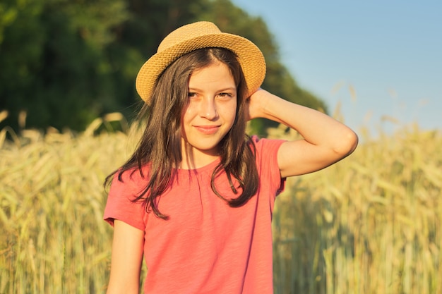 Retrato de hermosa niña con sombrero en campo de trigo