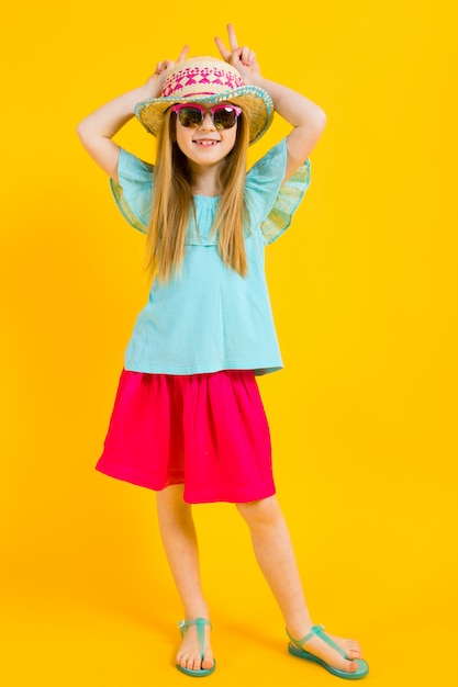 Retrato de una hermosa niña en un sombrero, gafas de sol, vestido de verano y sandalias.