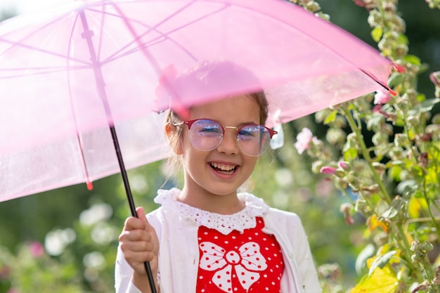 Retrato de una hermosa niña sonriente con gafas, bajo un paraguas rosa