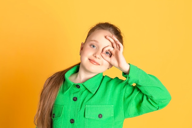 Retrato de una hermosa niña sonriente con el pelo largo una niña con un traje verde sobre un fondo amarillo en el estudio muestra el lugar de las emociones para el texto