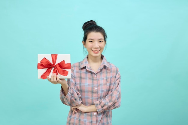 Retrato de una hermosa niña sonriente sosteniendo una caja de regalo y mirando a cámara aislada sobre fondo azul.