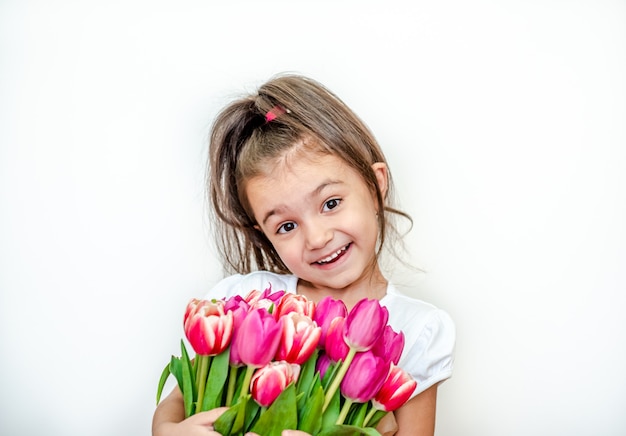 Retrato de una hermosa niña sonriente con tulipanes de primavera sobre un fondo blanco.