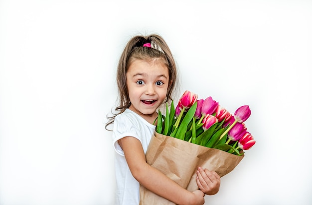 Retrato de una hermosa niña sonriente con tulipanes de primavera sobre un fondo blanco.
