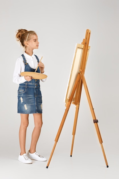 Retrato de una hermosa niña sosteniendo una paleta de arte de madera y un cepillo en el fondo del estudio