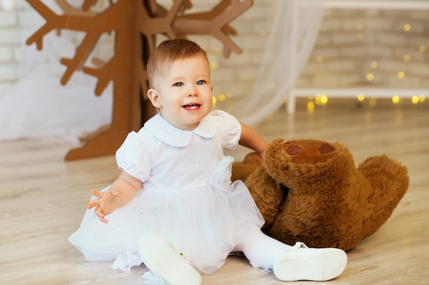 Retrato de una hermosa niña con un suave osito de peluche marrón en el interior con adornos navideños