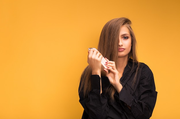 Retrato de una hermosa niña con un teléfono wooku sobre un fondo amarillo. La emoción fue pensativa.