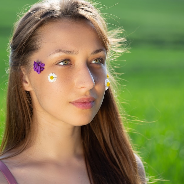 Foto retrato de una hermosa niña tranquila de pelo largo con flores silvestres en su rostro