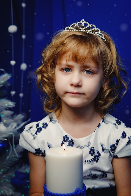 Retrato de una hermosa niña con velas en el fondo del árbol de Navidad