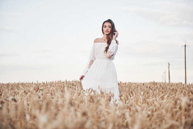 Retrato de una hermosa niña con un vestido blanco en el campo de trigo